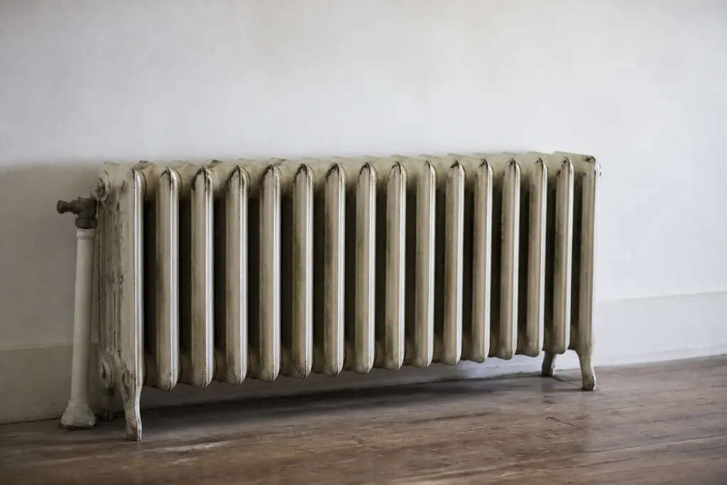 Vieux radiateur en fonte froid posé contre mur blanc
